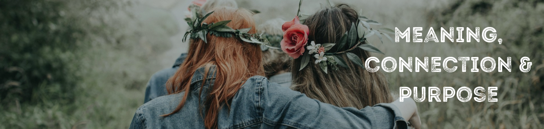 4 women facing away from the camera walking in pairs wearing flower headbands in the woods.