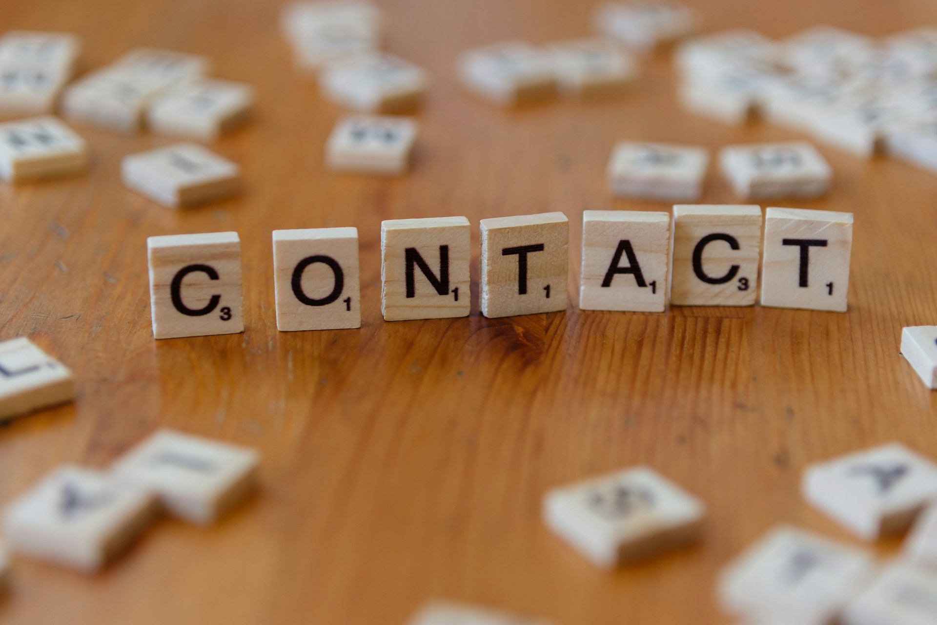 Scrabble pieces spelling out the word contact on a wooden table.