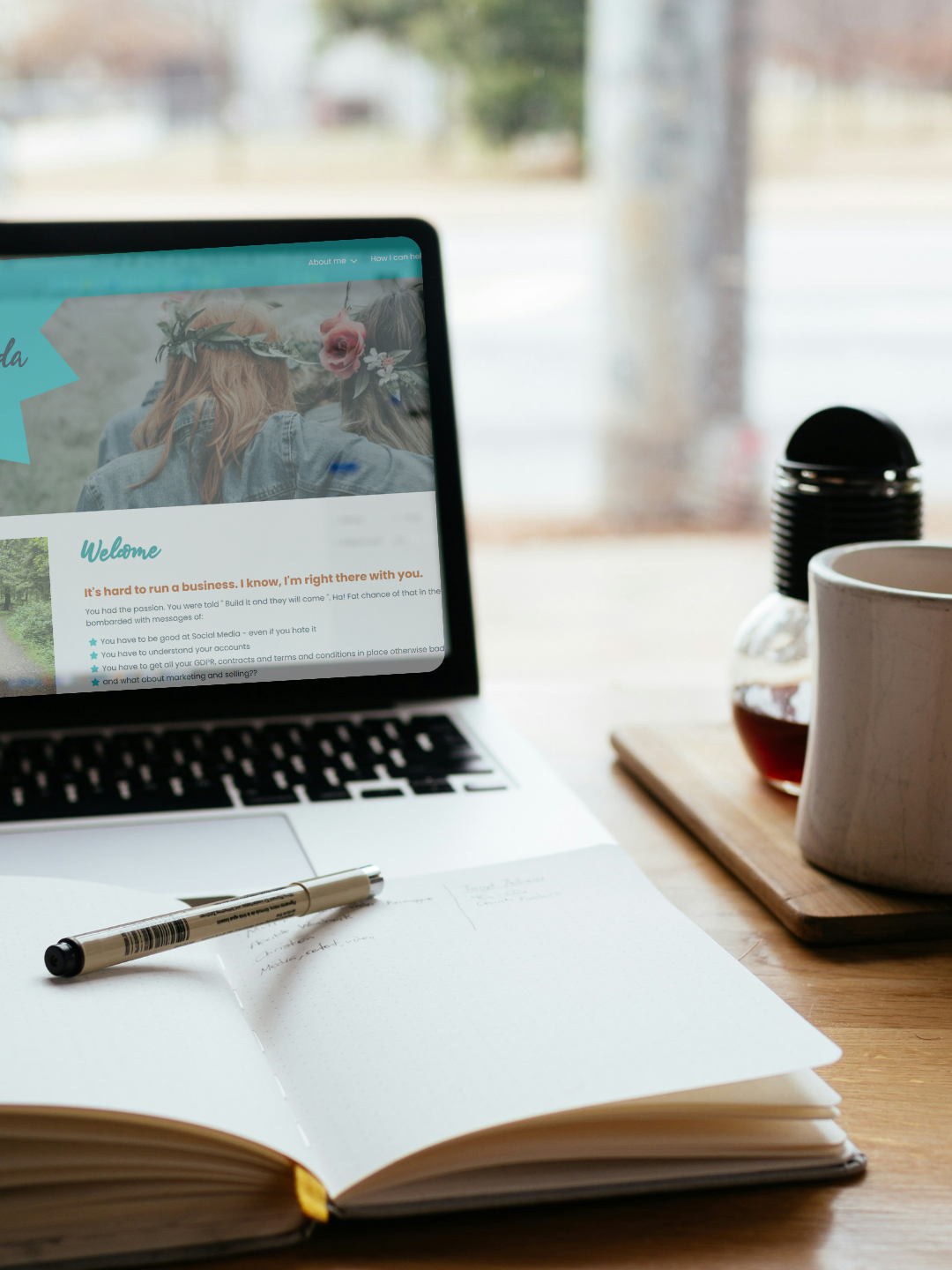 Laptop showing the Veda Coda Therapy website on a desk with a notepad in front of it.