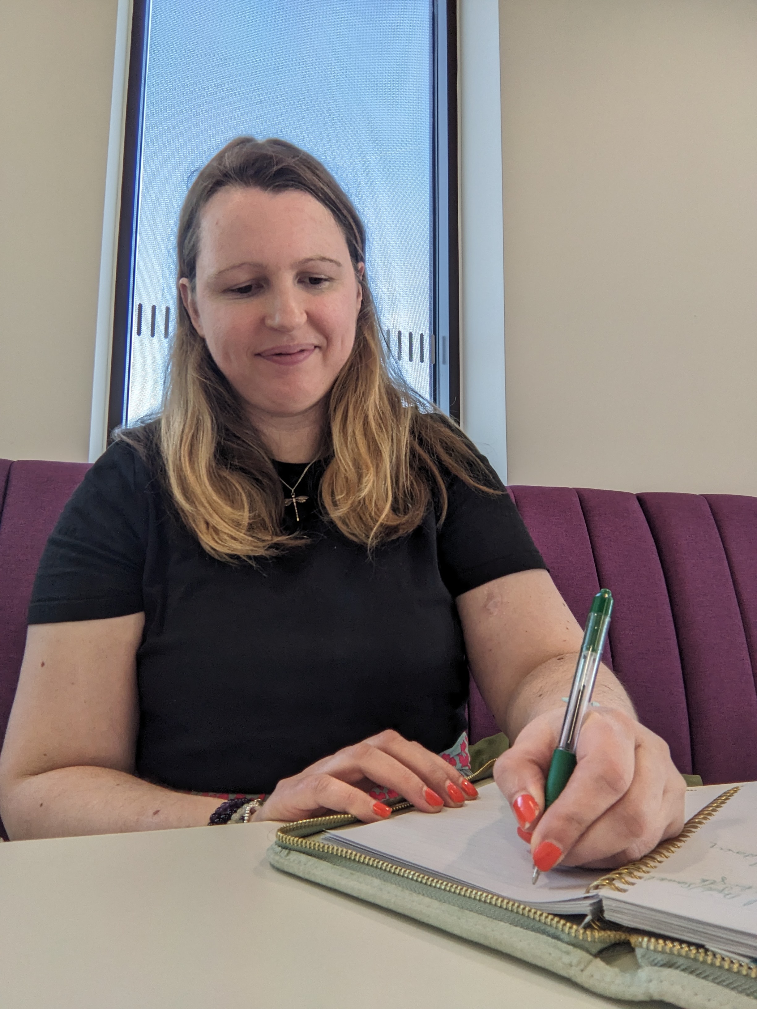Lindsay is sat at a table writing some notes.